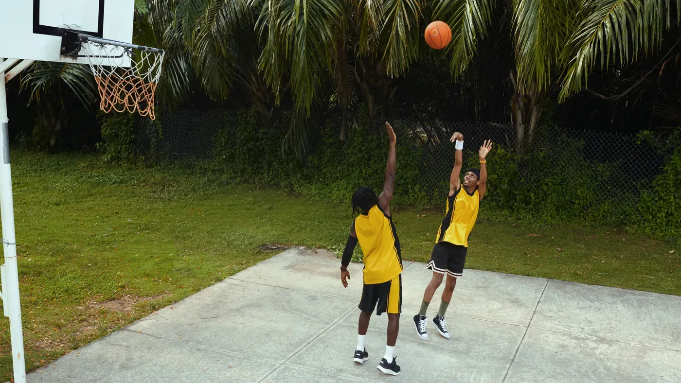 Två basketspelare hoppar mot korgen på en utomhusplan en solig dag