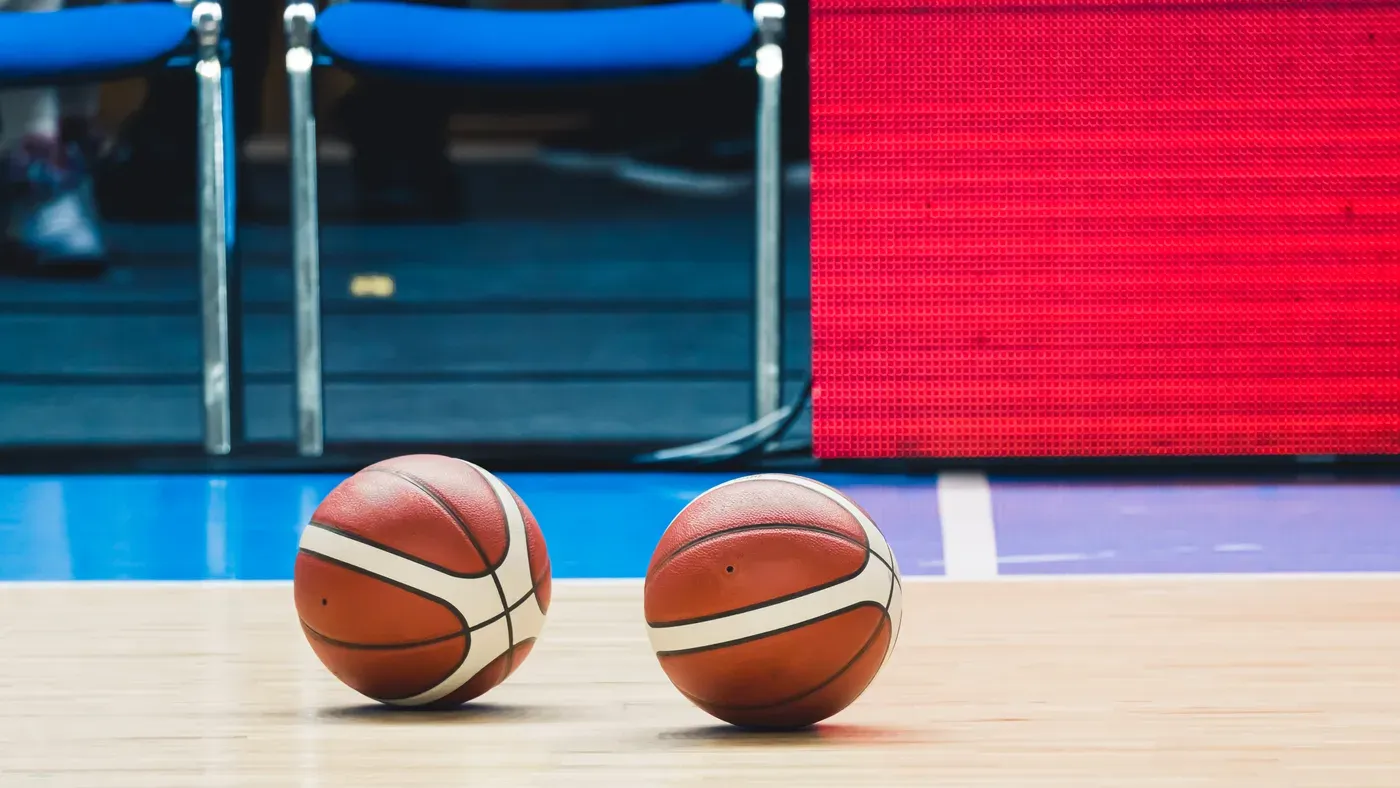 Två basketbollar ligger på golvet vid sidlinjen i en sporthall